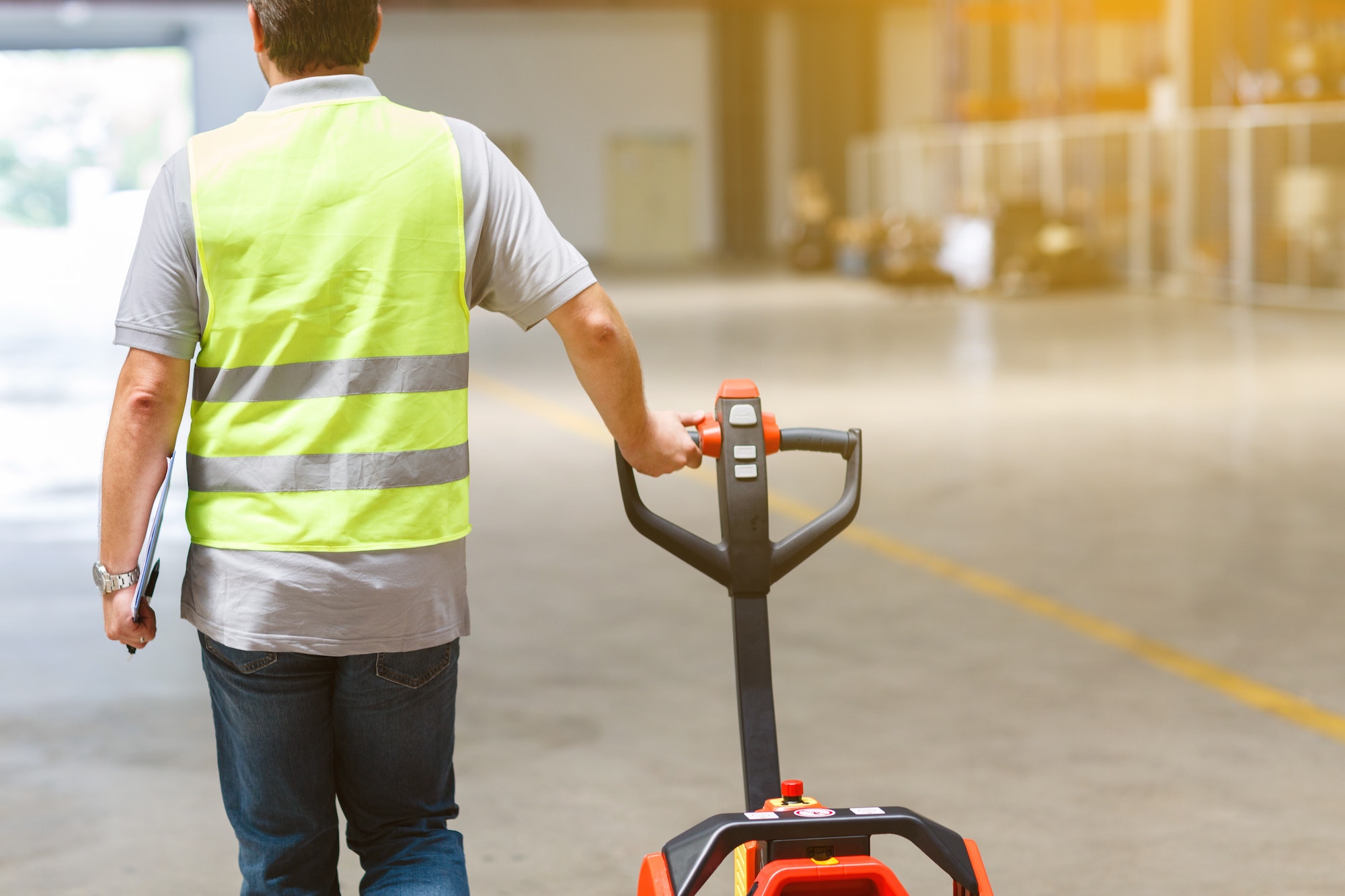 Werknemer van achteren aan het werk in een moderne fabriek of magazijn met behulp van een handpallettruck.